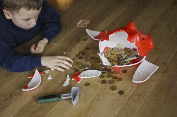 Symbolic photo on the subject of saving. A boy smashes his savings slip and counts the money it contains. Berlin, 10.02.2024