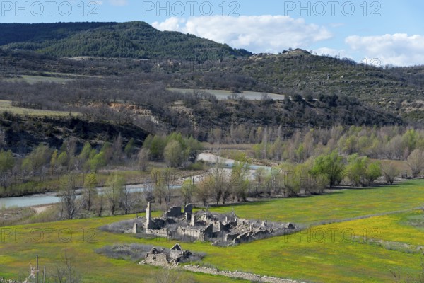 Ruins of an old building in a green field surrounded by a river and wooded hills on a clear spring day, Mas de Mont-rebei, Noguera Ribagorçana river, Lleida province, Catalonia, Aragon, Spain, Europe