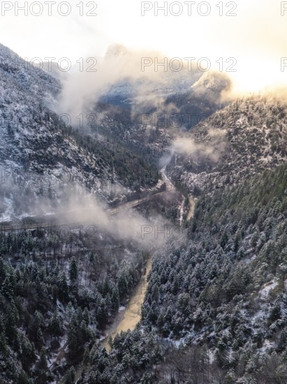 A valley with a river flowing through it surrounded by snow-covered mountains and wafts of mist, Alpenstraße, Bad Reichenhall, Germany, Europe