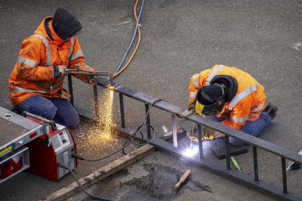 Locksmith at work, cutting and welding, on a workpiece in an industrial plant, a metal ladder is split with a welding torch, a welder fixes a ladder rung with a welding machine