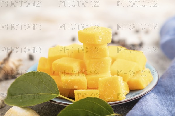 Dried and candied mango cubes on blue plate on brown concrete background and linen textile. Side view, close up, selective focus, vegan, vegetarian food concept