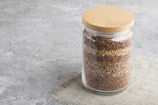 Glass jar with buckwheat poured in layers on a gray concrete background. side view, close up, copy space. Healthy food concept