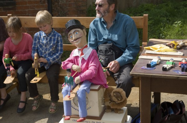 Man and children operating a traditional wooden jig doll dancer during a country folk event at Shottisham, Suffolk, England, United Kingdom, Europe