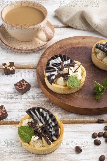 Sweet tartlets with chocolate and cheese cream with cup of coffee on a white wooden background and linen textile. side view, close up