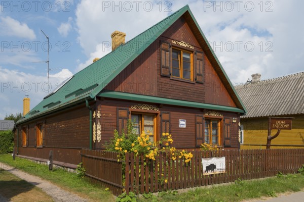 Dark brown wooden house with green roof and flowers in the garden behind the fence, Bialowieza, Bialowieza, Podlaskie Voivodeship, Podlaskie, Poland, Europe