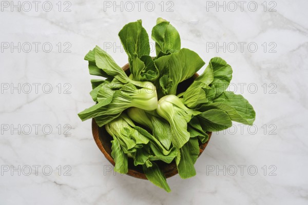 Vibrant green bok choy is neatly arranged in a rustic wooden bowl, set against a clean marble countertop bathed in soft, natural light, emphasizing the freshness and crispness of the vegetables.