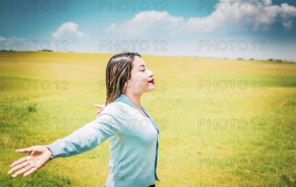 Happy girl spreading arms breathing fresh air in the field. Relaxed woman breathing fresh air in a beautiful field on a sunny day