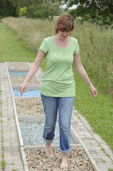 Woman walking barefoot over glass gravel and bottle corks, barefoot path Tilbeck Abbey, Havixbeck, North Rhine-Westphalia, Germany, Europe