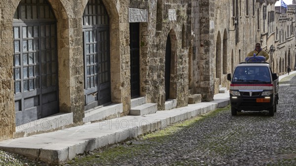 An old building with large windows along a cobblestone street and a moving small flatbed truck, Knights Street, Rhodes Old Town, Rhodes Town, Rhodes, Dodecanese, Greek Islands, Greece, Europe