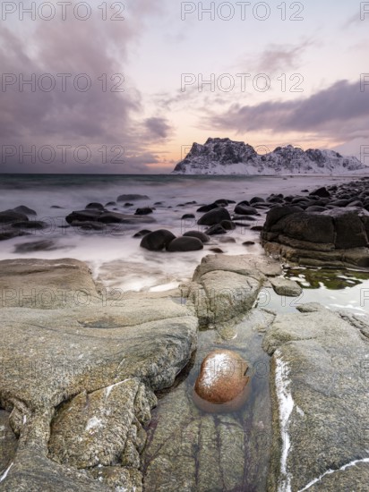 Rounded rocks on Utakleiv beach in a dramatic cloudy atmosphere, snow-capped mountains in the background, Vestvagoy Island, Lofoten, Norway, Europe