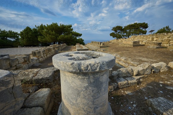 Stone column in the middle of an ancient ruins field with trees and stone structures in the background, Exedra, Kamiros, Archaeological site, Ancient city, Foundation of Doric Greeks, Rhodes, Dodecanese, Greek Islands, Greece, Europe