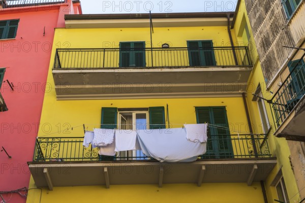 Yellow residential apartment building facade with washed clothes and blue bed sheet drying on clothesline in Riomaggiore, Cinque Terre, La Spezia province, Italy, Europe