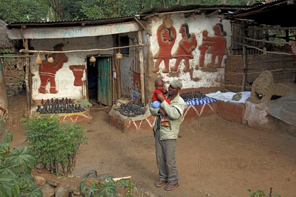 Amhara region, in the Falasha village of Wolleka near Gondar, Gonder, Jewish village, sale of home-made souvenirs, painted house, man with child in his arms, Ethiopia, Africa