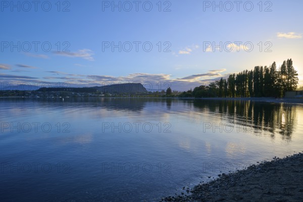 Clear lake with trees on the shore, sunrise and cloudy sky, calm scenery, summer, Lake Wanaka, Wanaka, Otago, South Island, New Zealand, Oceania