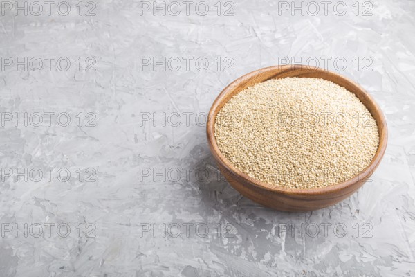 Wooden bowl with raw white quinoa seeds on a gray concrete background. Side view, close up, copy space