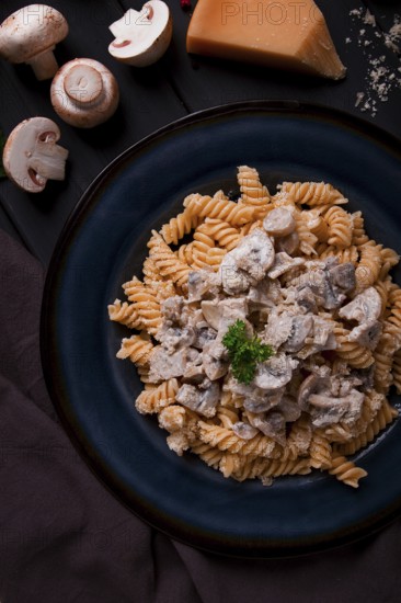 Fusilli pasta, with champignons in cream sauce, top view, with ingredients, on a wooden table, no people