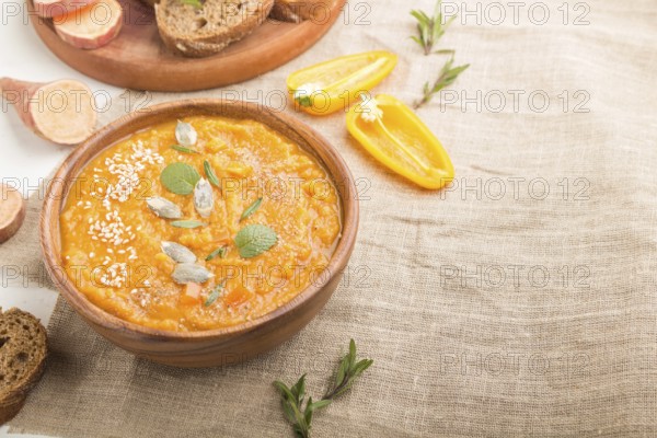 Sweet potato or batata cream soup with sesame seeds in a wooden bowl on a white wooden background with linen textile. side view, copy space, selective focus