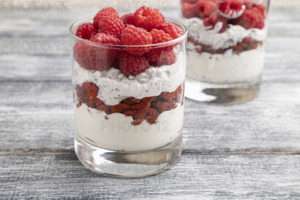 Yogurt with raspberry, goji berries and chia seeds in glass on gray wooden background. Side view, close up, selective focus