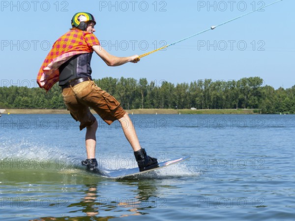 Young casual man with flapping shirt on wakeboard in lake, water ski and wakepark, Stráž pod Ralskem, Czech Republic, Europe