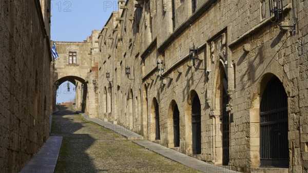 A historic alleyway with stone buildings and arches, blue and white flags in the background, Knights' Street, Rhodes Old Town, Rhodes Town, Rhodes, Dodecanese, Greek Islands, Greece, Europe