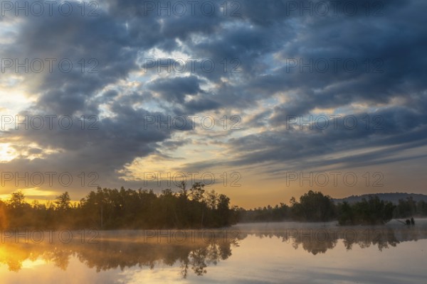 Fog over the lake at sunrise, dramatic clouds and reflecting water surface in natural surroundings, In the moor