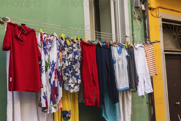 Men's and women's washed clothes drying on clothesline of green painted with white trim stucco cladded residential apartment building facade, Manarola, Cinque Terre, La Spezia province, Italy, Europe