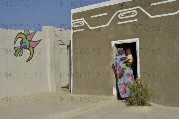 Woman carrying toddler, colorful painted Nubian house in the village Umogaal in Dongola, Nubia, Sudan, Africa