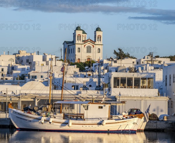 Fishing boats in the harbour at sunset, reflected in the sea, White Cycladic houses and church Agios Faneromeni, Naoussa, Paros, Cyclades, Greece, Europe