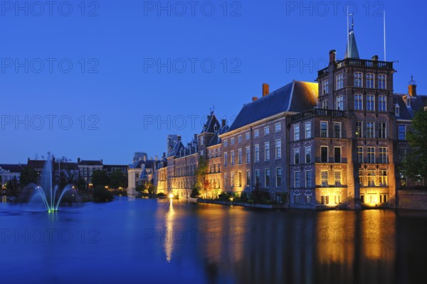 View of the Binnenhof House of Parliament and the Hofvijver lake with downtown skyscrapers in background illuminated in the evening. The Hague, Netherlands