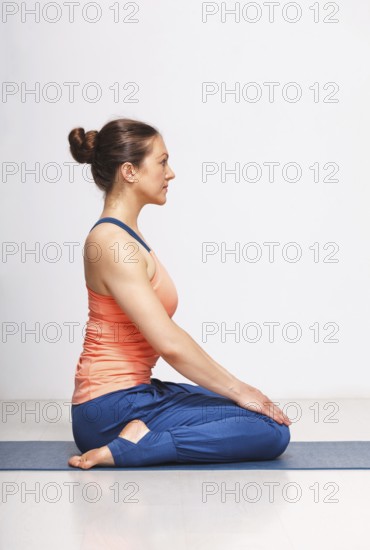 Woman in Hatha yoga asana Vajrasana, vajra pose or diamond pose on yoga mat on yoga mat in studio on grey bagckground