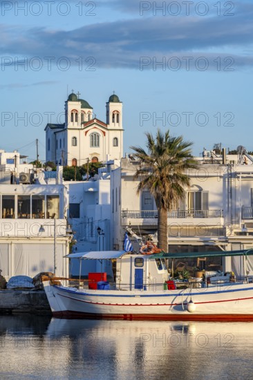 Fishing boats in the harbour at sunset, reflected in the sea, White Cycladic houses and church Agios Faneromeni, Naoussa, Paros, Cyclades, Greece, Europe