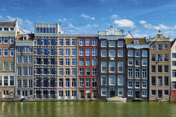 Row of typical houses and boat on Amsterdam canal Damrak with reflection. Amsterdam, Netherlands