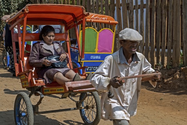 Old Malagasy man pulling pousse-pousse, pulled rickshaw with local woman in the city Antsirabe, Vakinankaratra, Central Highlands, Madagascar, Africa