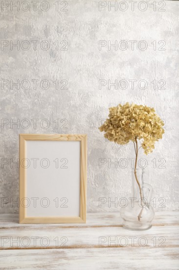 White wooden frame mockup with dried hydrangea in glass on gray concrete background. Blank, vertical orientation, still life, copy space