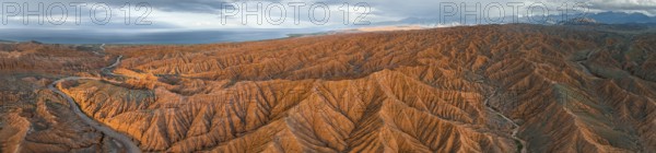 Panorama, landscape of eroded hills, badlands at sunset, behind mountain peaks of the Tian Shan Mountains and Issyk Kul Lake, aerial view, Canyon of the Forgotten Rivers, Issyk Kul, Kyrgyzstan, Asia