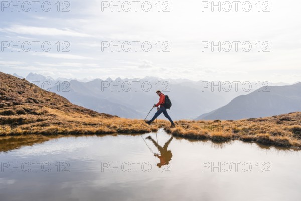 Mountaineer hiking with poles, reflected in a small mountain lake on the Krahberg, mountain panorama in autumn, Venet crossing, Ötztal Alps, Tyrol, Austria, Europe