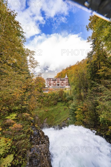 A river flows through an autumnal forest landscape with a hotel in the background under a cloudy sky, Lake Brienz, Giessbach Waterfall, Switzerland, Europe