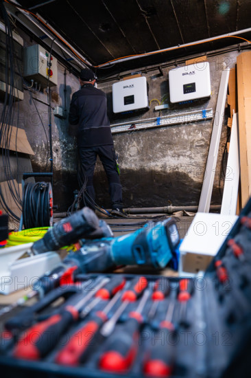 Close-up of tools in the foreground while electricians install Solax devices