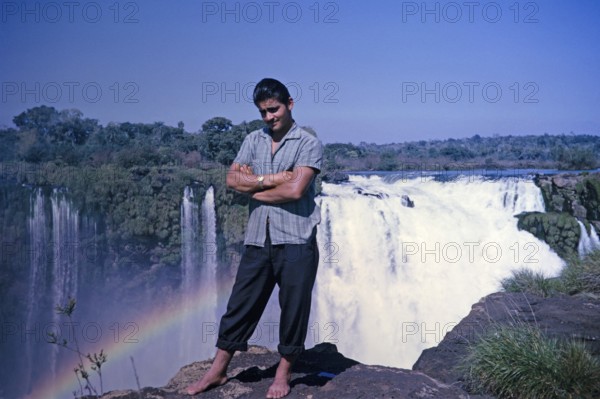 Male tour guide standing barefoot at the edge of the Iguazu Falls on the Iguazu River, on the border between Brazil and Argentina, South America, 1962