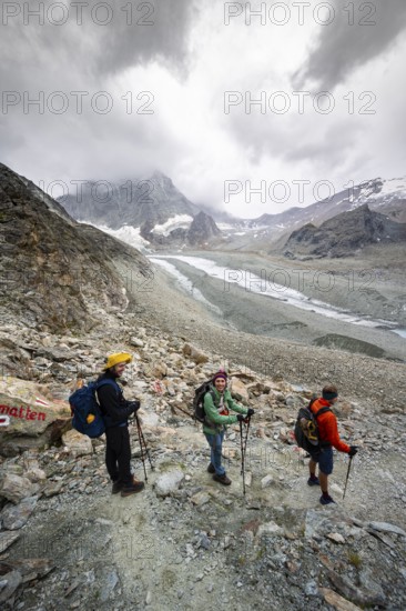 Group of mountaineers descending from Col de Riedmatten, view of glacier Glacier de Cheilon and mountain peak Mont Blanc de Cheilon, with dark clouds, Valais, Western Alps Switzerland