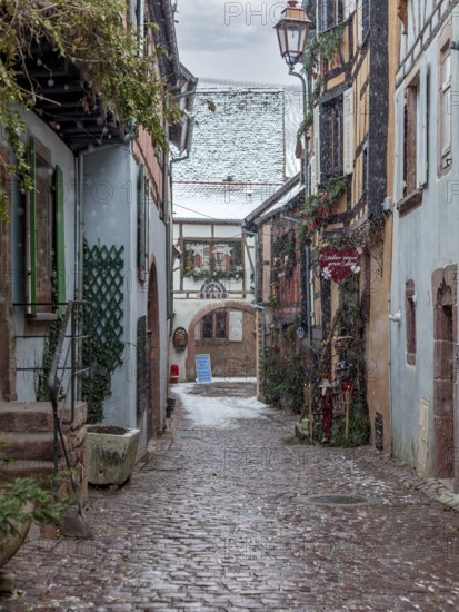 Narrow alley with half-timbered houses and cobblestones in a wintery and quiet atmosphere during snowfall, Alsace, France, Europe