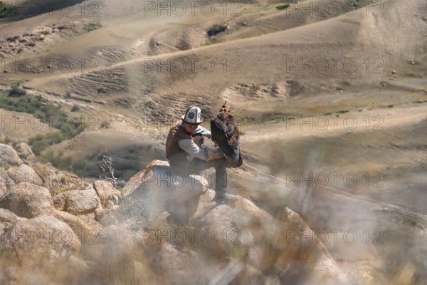 Traditional Kyrgyz eagle hunter hunting in the mountains in a dry landscape, near Kysyl-Suu, Issyk Kul, Kyrgyzstan, Asia