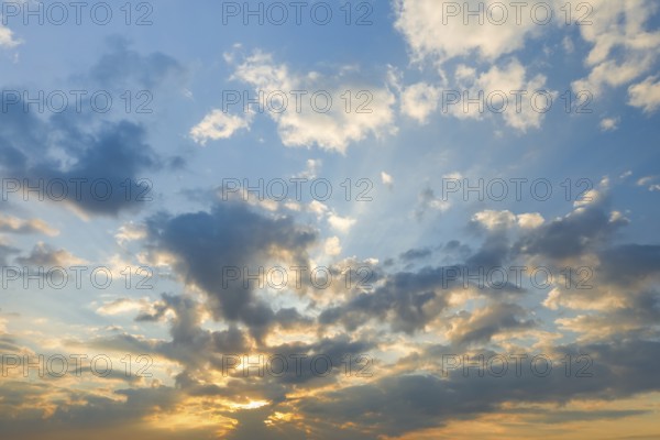 Sun breaks through cloud cover and illuminates fleecy clouds in the evening blue sky