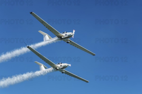 Stunt aerobatic plane performing stunts in blue sky with smoke trail. Concept of teamwork, collaboration, coordination, trust, precision, difficulty, challenge, speed, synergy