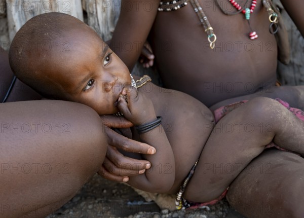 Himba baby lies in the arms of his sister, near Opuwo, Kaokoveld, Kunene, Namibia, Africa