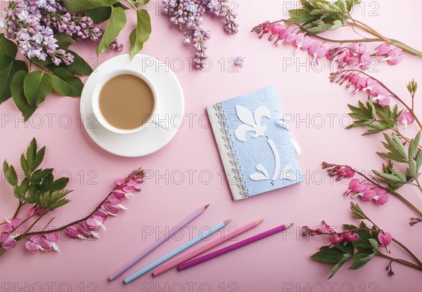 Purple lilac flowers and a cup of coffee with notebook and colored pencils on pastel pink background. Morninig, spring, fashion composition. Flat lay, top view