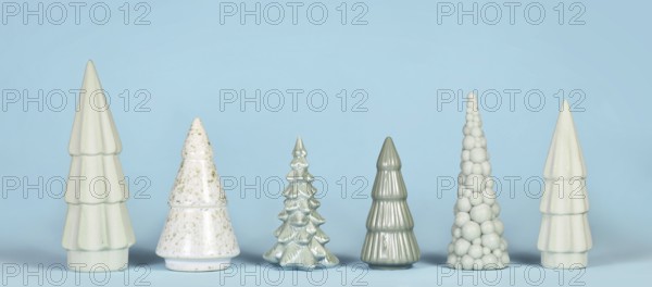 Banner with different shaped light green ceramic Christmas trees on blue background