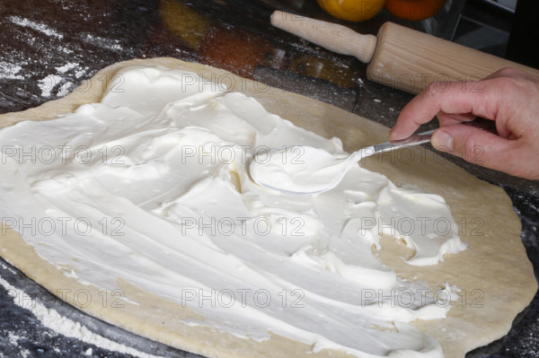 Swabian cuisine, preparation of savoury yeast plait with smoked meat, salty wreath bread, yeast yeast dough pastries, spread raw yeast dough with sour cream, behind rolling pin, grandmother's kitchen, regional, home cooking, typical Swabian cuisine reinterpreted, traditional cuisine reinterpreted, men's hands, food photography, studio, Germany, Europe