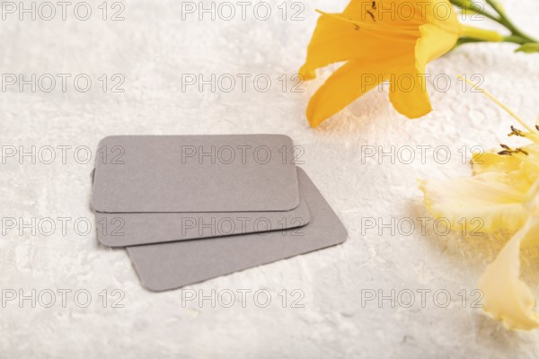 Gray paper business card mockup with orange day-lily flower on gray concrete background. Blank, side view, copy space, still life. spring concept