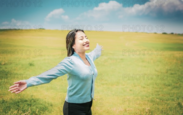 Serene young woman breathing fresh air in beautiful field spreading arms. Happy girl spreading arms breathing fresh air in the field